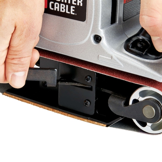 Close-up of hands adjusting the lever on a PORTER-CABLE belt sander, showing the sanding belt and part of the machine's metallic body.