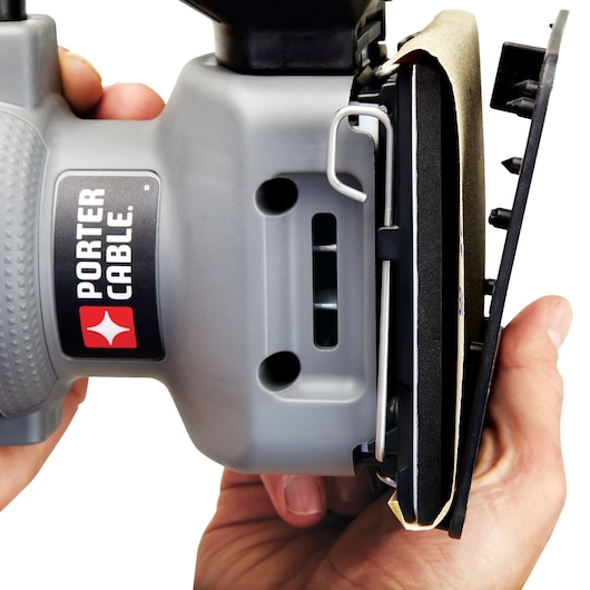 Close-up view of a PORTER-CABLE hand-held power sander being held, showing its side and sanding pad with sandpaper attached.