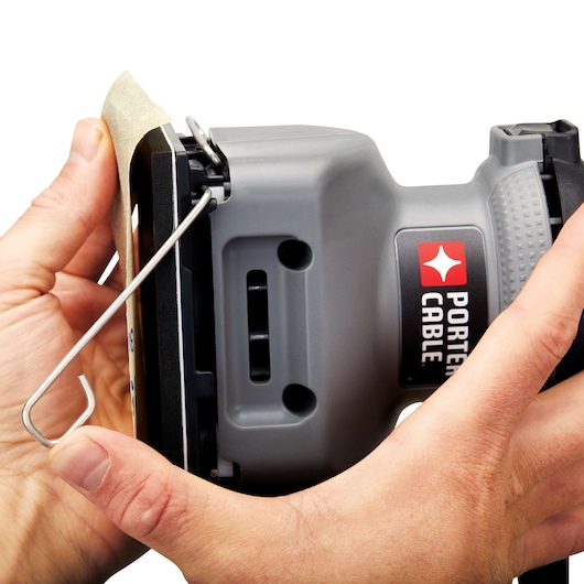 Close-up of hands attaching sandpaper to a PORTER-CABLE electric sander, showing the brand logo and clamp mechanism.
