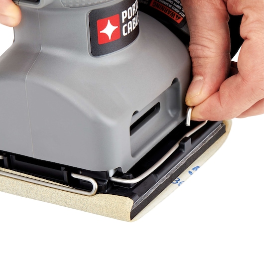 Close-up of a person's hand adjusting a clamp on a PORTER-CABLE power sander, securing sandpaper to the tool.