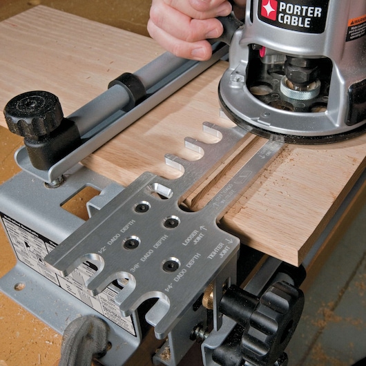 A PORTER-CABLE woodworking dovetail jig is being used with a router to create joints in a piece of wood, showing detailed metal guides and adjustment knobs.