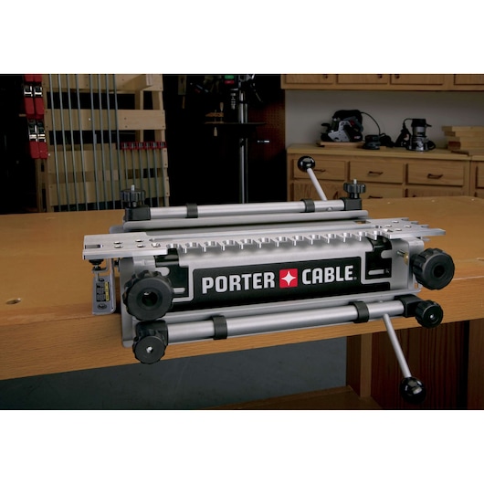 A Porter-Cable 4210 dovetail jig mounted on a woodworking bench in a workshop. The tool is designed for creating precise joinery and features adjustment knobs and metal guides.