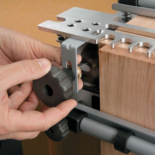 Close-up of a person adjusting a PORTER-CABLE dovetail jig, securely holding a piece of wood in place with a metal clamp and a large black knob.