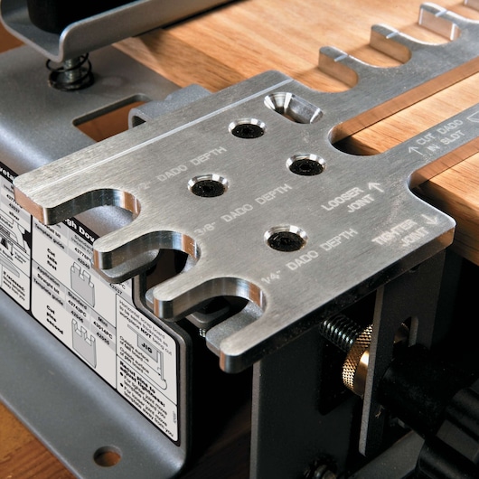 Close-up view of a PORTER-CABLE dovetail jig tool used in woodworking. The metal template has labeled cut slots for dado depth, joint tightness adjustments, and is mounted next to a piece of wood. The base features instructional diagrams for various joint types.