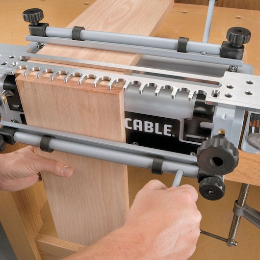 A person is using a PORTER-CABLE 4212 woodworking jig to hold two wooden boards in place, preparing them for joinery on a workbench.