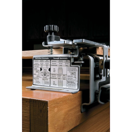 Close-up image of a PORTER-CABLE dovetail jig (model 4216) clamped to the edge of a wooden workbench. The jig features metal components and an instructional guide plate that provides information for making half-blind and through dovetail joints.