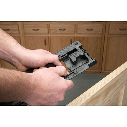 A close-up view of someone using a PORTER-CABLE door hinge template tool to mark or cut a hinge location on a wooden door, with cabinets in the background.