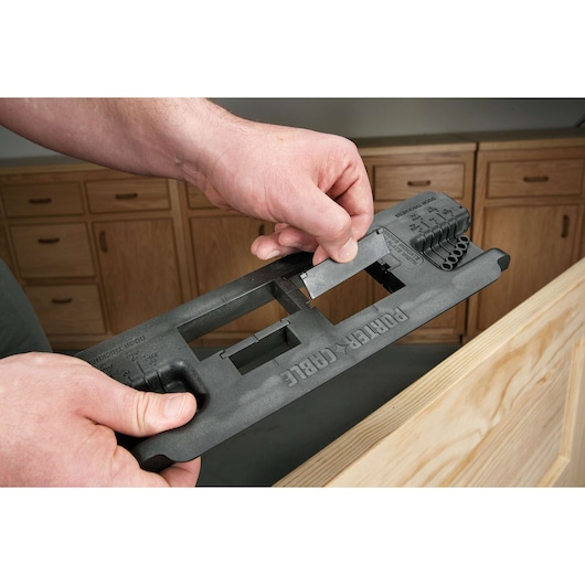 A person is holding a PORTER-CABLE door hinge template tool in a workshop, positioning it on a wooden door to assist with hinge installation.