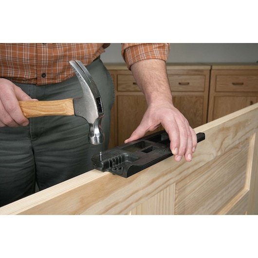 A person uses a hammer and a PORTER-CABLE tool to work on a wooden door. The tool is positioned on the edge of the door to assist with nail placement.