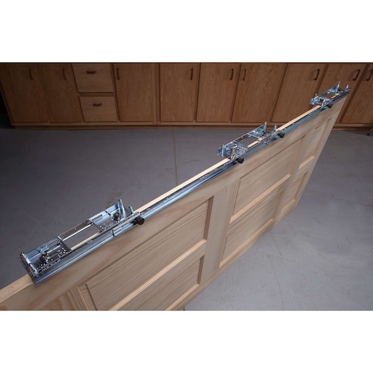 A PORTER-CABLE door hardware jig mounted on the edge of a wooden interior door, shown in a workshop with cabinets in the background.