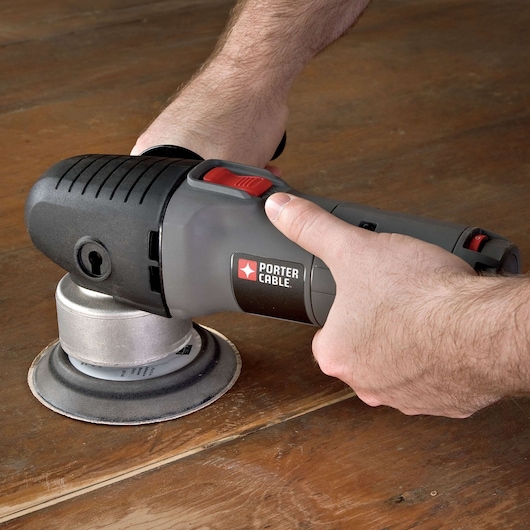 A close-up of hands using a PORTER-CABLE power sander on a wooden surface.