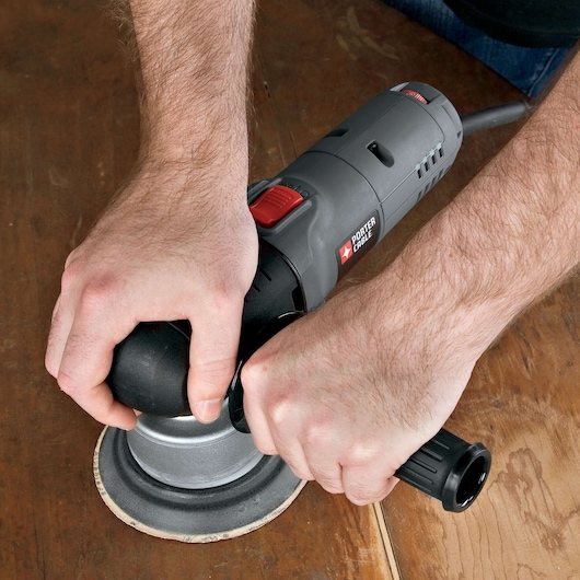 A person is using a PORTER-CABLE model 7345 electric sander to smooth the surface of a wooden table.