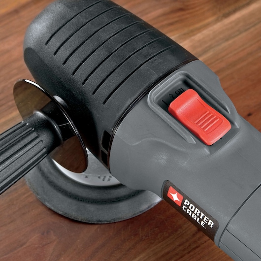Close-up view of a PORTER-CABLE power tool with a black handle, a red power switch, and a sanding or polishing pad, placed on a wooden surface.