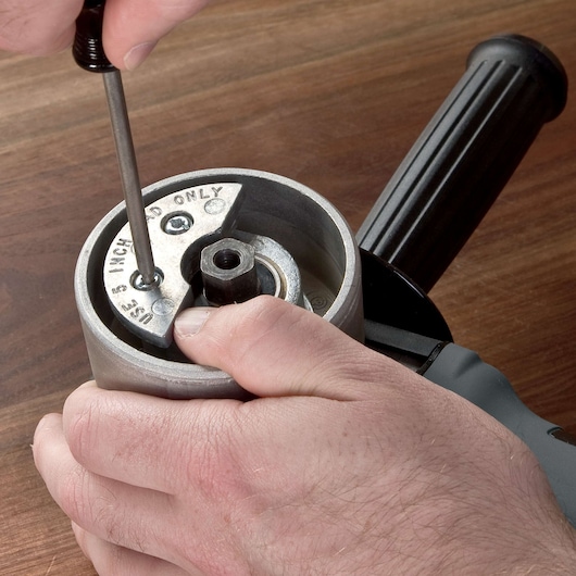 Close-up of a person using a screwdriver to adjust or assemble a part on a PORTER-CABLE power tool, likely a sander or grinder, on a wooden surface.
