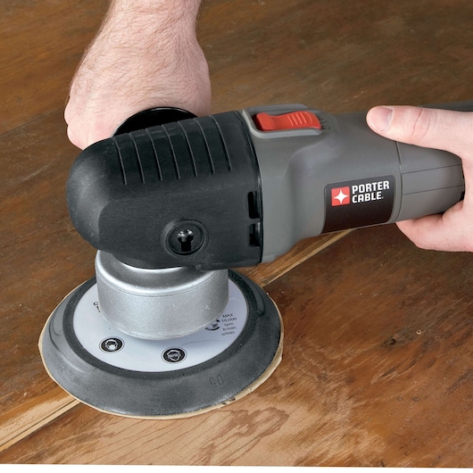 A PORTER-CABLE branded handheld sander being used on a wooden surface by a person.