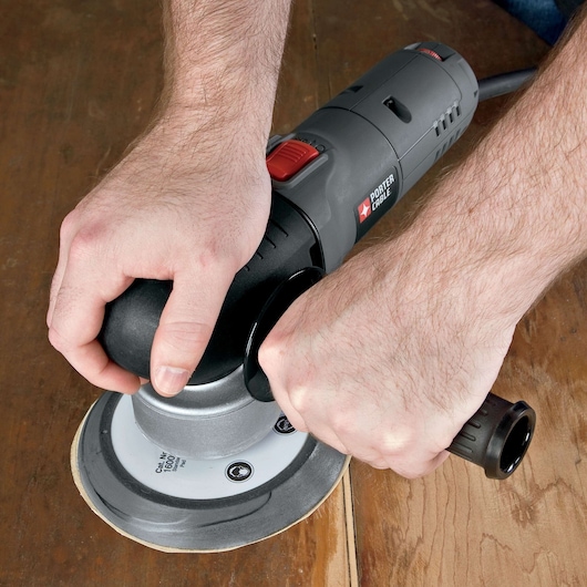A person is using a PORTER-CABLE electric sander (model 7346SP) to sand a wooden surface.