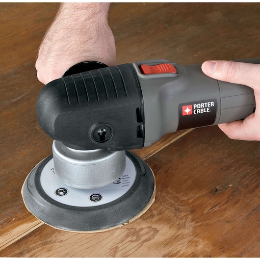 A close-up of a person using a PORTER-CABLE electric sander to smooth a wooden surface.