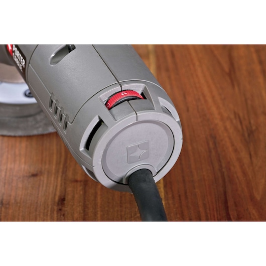Close-up view of the rear part of a PORTER-CABLE power tool with a gray plastic casing, visible cord, and a red dial. The tool is placed on a wooden surface.