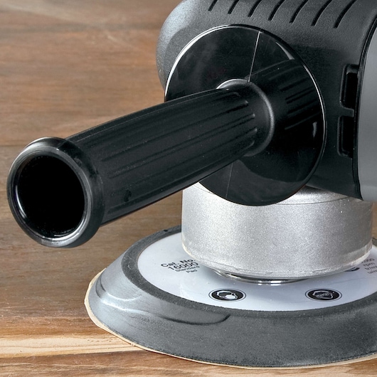 Close-up view of a PORTER-CABLE power tool, featuring a black side handle and a round sanding pad resting on a wooden surface.