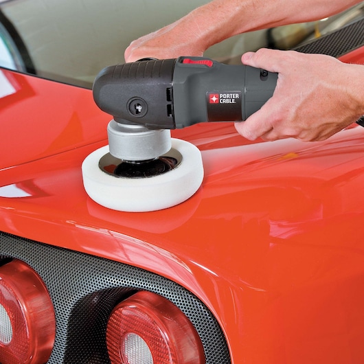 A person uses a PORTER-CABLE 7424XP variable speed polisher with a foam pad to polish the surface of a red car, focusing on the area near the rear lights.
