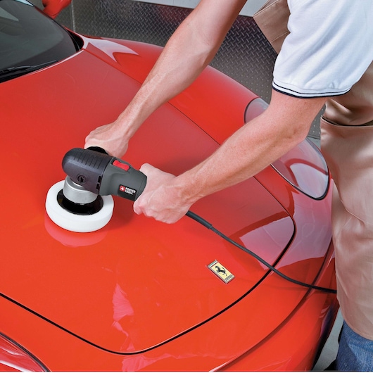 A person uses a PORTER-CABLE 7424XP polisher on the hood of a red car, with a white polishing pad attached. The car's surface is being polished for a smooth and shiny finish.