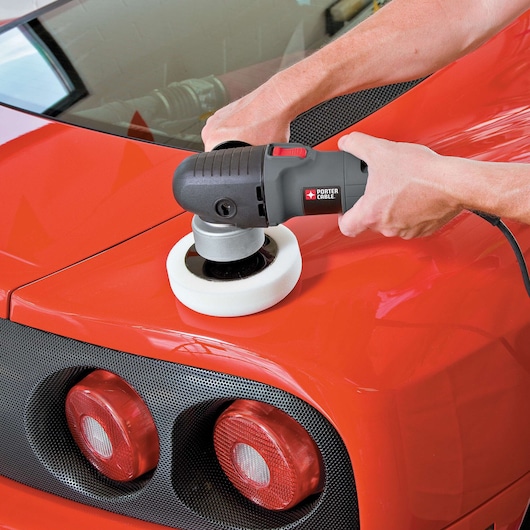 A PORTER-CABLE 7424XP electric polisher is being used to polish the rear surface of a red car, focusing on the area near the taillights.