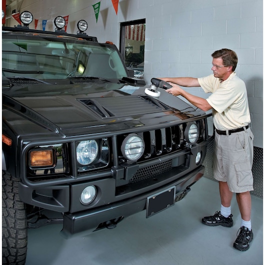 A person uses a PORTER-CABLE 7424XP polisher on the hood of a large black SUV inside a garage or showroom. The person's face is blurred for privacy.