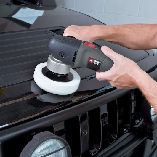 A person is using a PORTER-CABLE 7424XP polisher on the hood of a black vehicle, demonstrating car surface polishing.