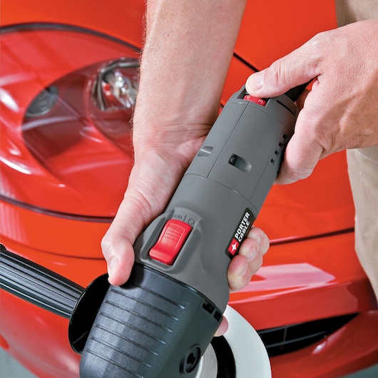 A person holding a PORTER-CABLE model 7424XP polisher, using it on the surface of a shiny red car.