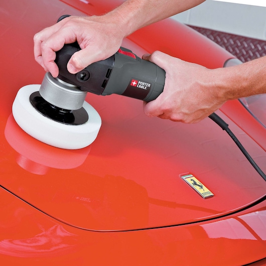 A person is using a PORTER-CABLE 7424XP electric polisher with a white foam pad to polish the hood of a shiny red car.