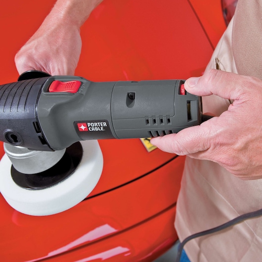 A person is holding a PORTER-CABLE 7424XP polisher, using it on a red car's surface.