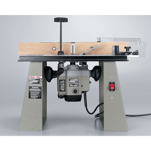 A Porter-Cable router table with a mounted router, featuring a wooden guide fence, metal legs, and a power switch on the right leg. The tool is designed for woodworking and precision routing tasks.