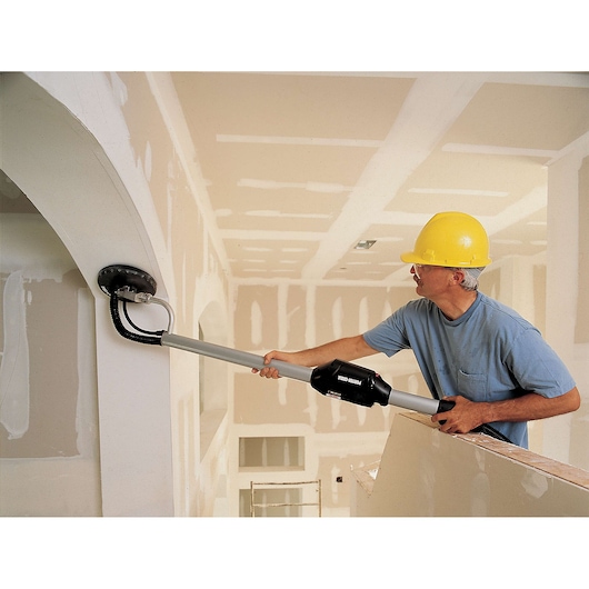 A person wearing a yellow hard hat and blue shirt is using a PORTER-CABLE drywall sander (model 7800) to sand a curved wall in a room that is under construction, with unfinished drywall surfaces visible.