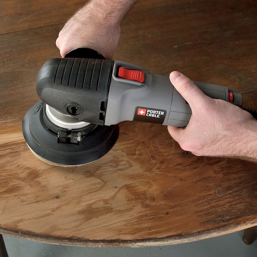 A person is using a PORTER-CABLE electric sander to smooth the surface of a wooden table.