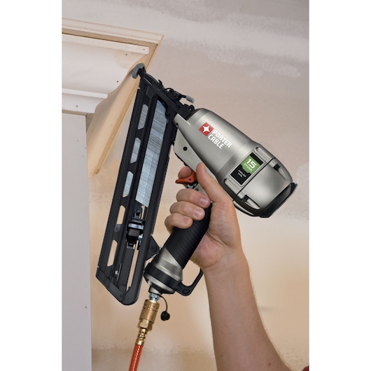 A close-up of a hand holding a PORTER-CABLE DA250C pneumatic nail gun, used to install trim or molding on a wall.