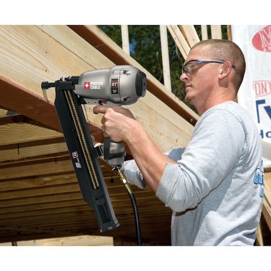 A person using a PORTER-CABLE 21-degree pneumatic framing nailer (model FR350B) on a wooden construction project. The tool is connected to an air hose and is being used to fasten wood beams.
