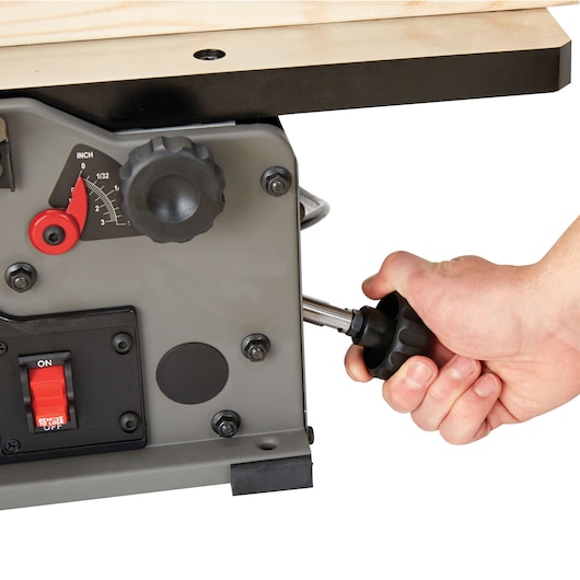 Close-up of a person adjusting a knob on the side of a PORTER-CABLE woodworking jointer, with a power switch and measurement dial visible.