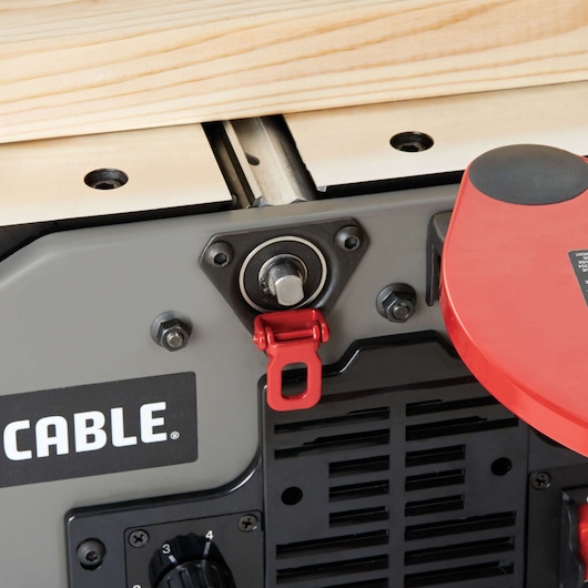 Close-up view of a PORTER-CABLE woodworking jointer machine with a wooden board placed on top. Visible are the adjustment knob, red clamp, and part of a safety guard.