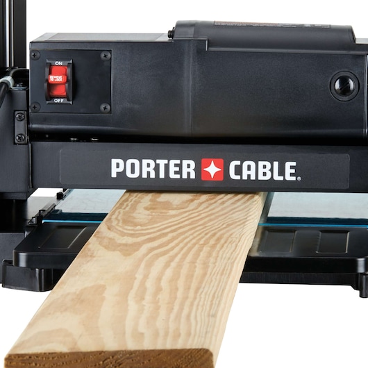 A PORTER-CABLE woodworking planer machine in use, with a piece of wood being processed through it. The machine features a red power switch and displays the brand logo on the front.
