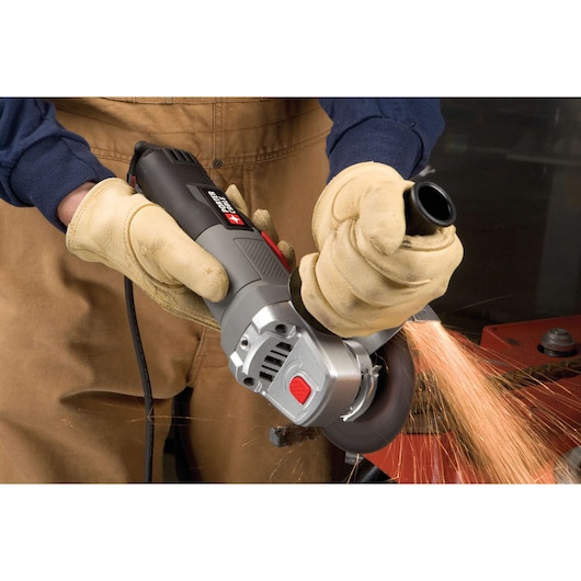 A person wearing gloves operates a PORTER-CABLE angle grinder, cutting metal and producing sparks. The tool is being held firmly with both hands near a workshop setting.