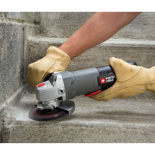 A close-up of a person wearing work gloves using a PORTER-CABLE angle grinder to smooth or grind the edge of a concrete step.