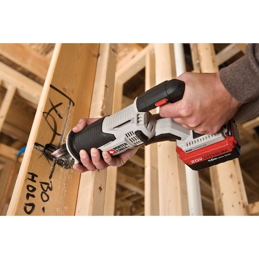 A person using a PORTER-CABLE 20V lithium-ion cordless reciprocating saw (model PCC670B) to cut through a wooden beam inside a construction site.