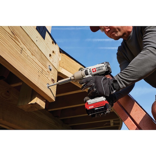 A person using a PORTER-CABLE 20V Lithium cordless impact driver to drive a screw into wooden beams at a construction site.