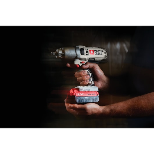 A person holds a PORTER-CABLE 20V lithium cordless impact wrench with a red and black battery pack. The tool is shown against a dark background.