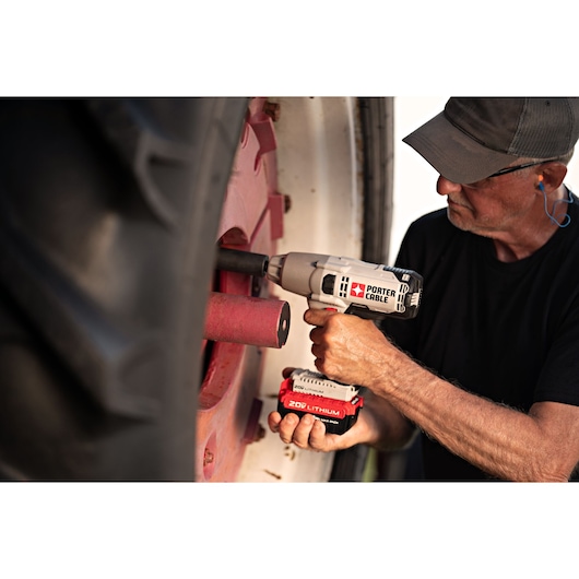 A person using a PORTER-CABLE PCC740LA 20V Lithium cordless impact wrench to work on the wheel of a large vehicle. The user's face is blurred for privacy.