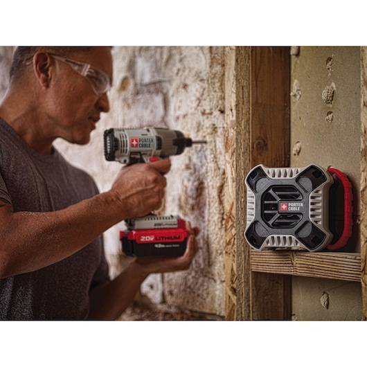 A PORTER-CABLE portable radio is mounted on a wooden beam at a construction site, while a person uses a PORTER-CABLE cordless power drill on a stone wall nearby. The radio and drill both feature visible brand logos.