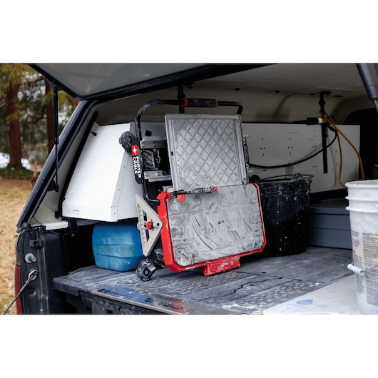 A PORTER-CABLE tile saw (model PCC780LA) covered in dust and residue is placed in the back of a work vehicle or truck. The saw is surrounded by various work tools, buckets, and containers, indicating an active job site or transportation for construction work.