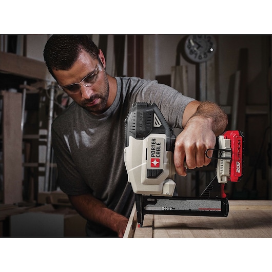 A person using a PORTER-CABLE 20V Lithium battery-powered nailer tool to fasten wood in a workshop. The person's face is obscured.
