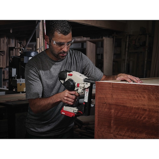 A person using a PORTER-CABLE 20V cordless nailer (SKU: PCC791LA) to work on wooden furniture in a workshop. The person's face is obscured for privacy.