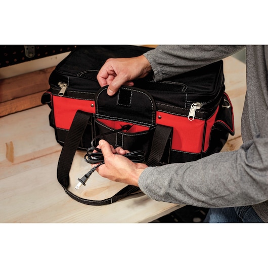 A person holding a power cord next to a black and red tool bag placed on a wooden surface.